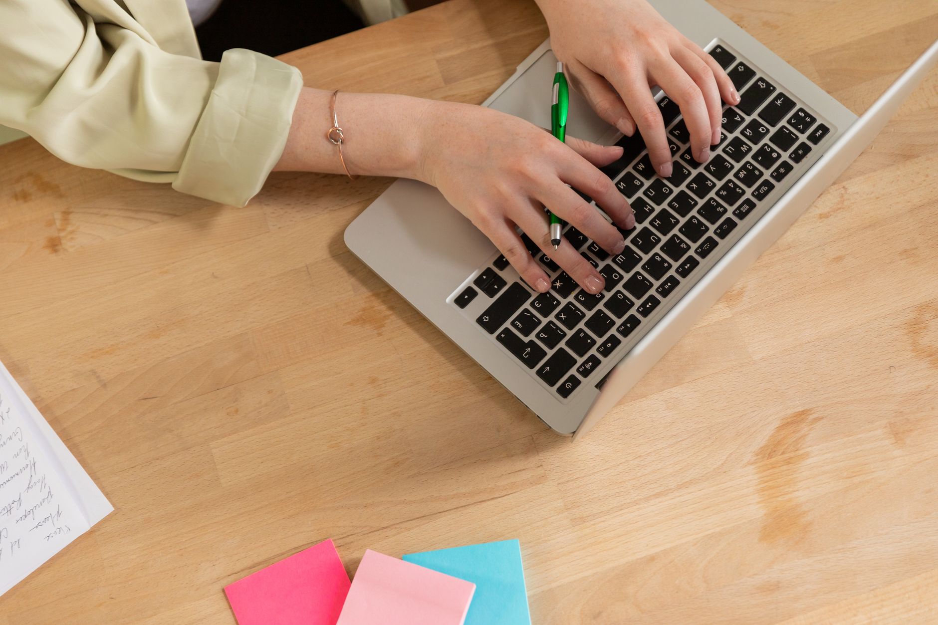 Hands typing on a laptop with a green pen and colorful sticky notes on a wooden desk — illustrating: Top 7 Managed IT Service Providers for Tampa Bay & Central Florida SMBs: An Honest Comparison