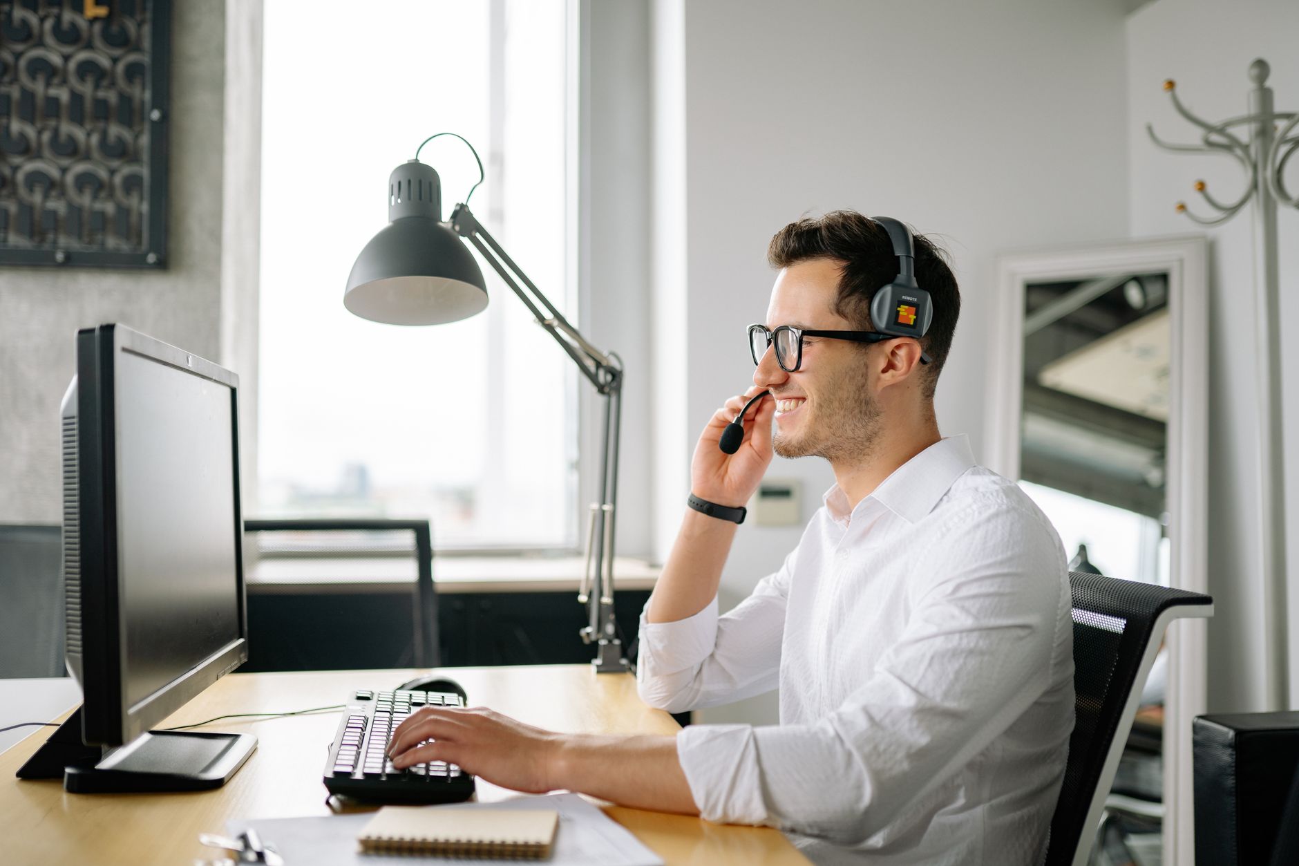 Smiling man wearing headset working at computer in bright office — illustrating: Tampa Business Phone Systems: VoIP vs Traditional Phone Lines Compared — A Central Florida SMB Guide